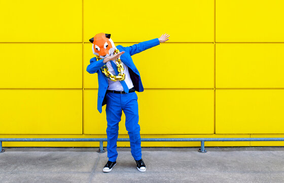 Man wearing vibrant blue suit and tiger mask dabbing in front of yellow wall