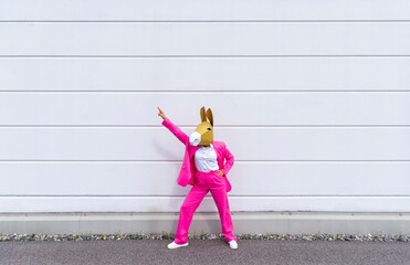 Woman wearing vibrant pink suit and donkey mask posing in front of white wall