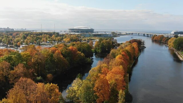 Aerial view of the autumn park and the Zenit Arena sports stadium in St. Petersburg and Krestovsky island with a pier and yachts all-sunny day. Bright colors of the autumn city park.