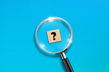 Magnifying glass and question mark on wooden block with blue background