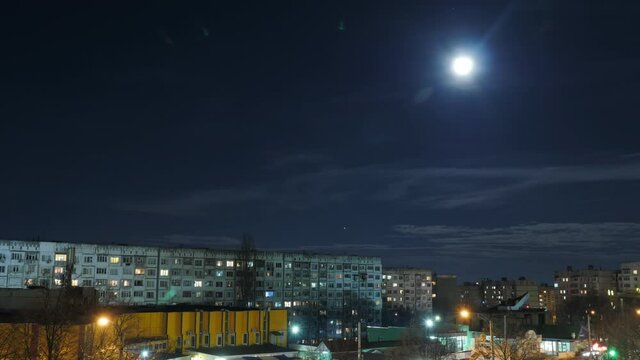 Time lapse. Full moon rises over top of old communist era buildings, at night.