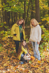 Naklejka na ściany i meble Portrait of three generations of happy beautiful women and dog looking at camera, hugging and smiling in autumn nature.