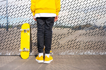 Male skater wearing yellow shoes standing by skateboard in front of metallic wall