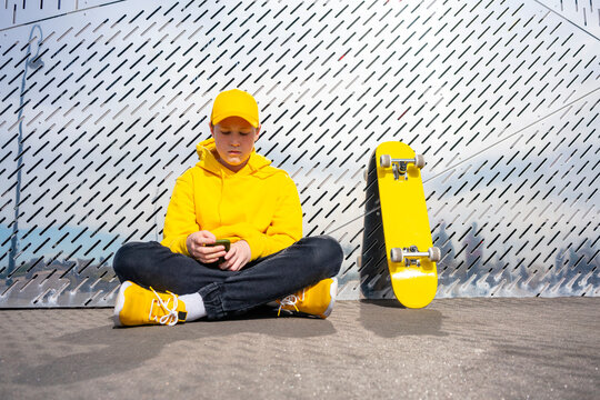 Lonely male skater using smart phone by yellow skateboard