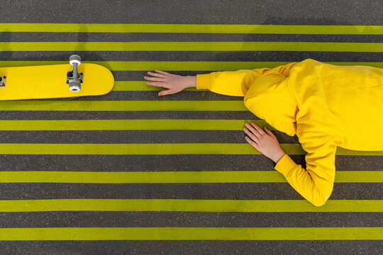 Boy reaching for skateboard while lying on yellow road markings