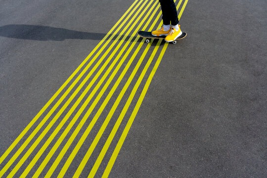 Boy with skateboard over yellow road markings on sunny day