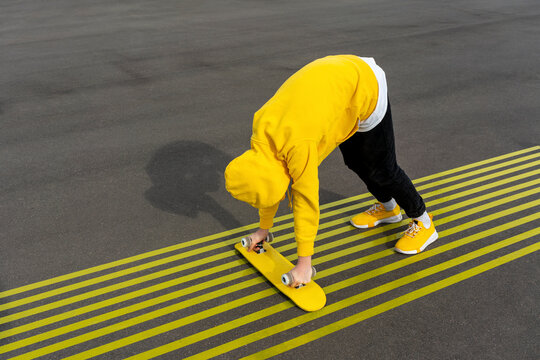 Boy holding skateboard while bending over yellow markings on road