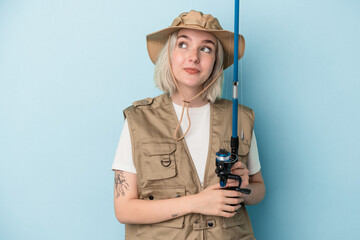 Young caucasian fisherwoman holding a rod isolated on blue background dreaming of achieving goals and purposes