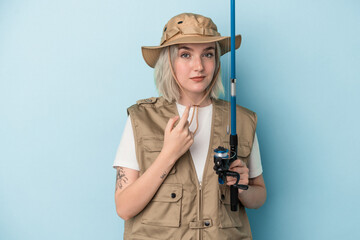 Young caucasian fisherwoman holding a rod isolated on blue background pointing with finger at you as if inviting come closer.