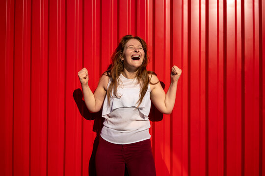 Cheerful young redhead woman laughing in front of red corrugated wall