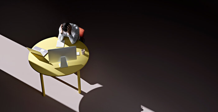 Businessman sitting alone at table in darkened room with head in hands