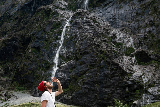 New Zealand, South Island, Fiordland National Park, Young man pretending to drink waterfall