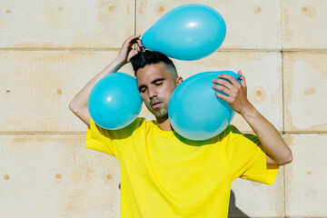 Young man holding blue balloons near wall