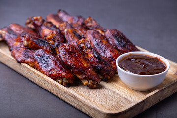 Fried chicken wings on a wooden board with barbecue sauce. Black background, close-up.