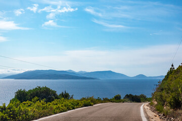 Driving high steep road with green vivid hills, blue distant islands silhouettes and clear blue...
