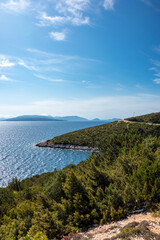 Fototapeta na wymiar Green cliffs on sunny sea shore on a bright clear blue day in Greece. Sun beam on water and blue sky, Lefkada island, Ionian sea coast. Vertical