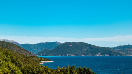 Fototapeta na wymiar Panorama on greenery cliffs, sunny sea shore on a bright clear blue day in Greece. Scenic travel destination. Lefkada island, Ionian sea coast