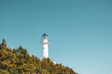 Ionian sea island lighthouse on green cliff on a bright clear blue sky in Greece. Scenic travel destination. Lefkada island. Color graded