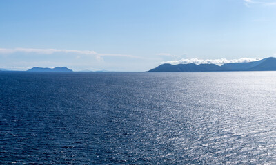 Blue Mediterranean panorama. Ionian sea landscape view on Lefkada Greece island. Bright day with low clouds over distant islands and contrast sunbeam on water