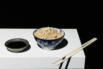 Bowl of white rice with chopsticks with soy sauce on the white shelf