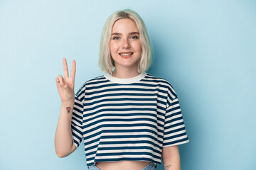 Young caucasian woman isolated on blue background joyful and carefree showing a peace symbol with fingers.