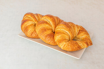 Tray with three butter croissants for breakfast on white table