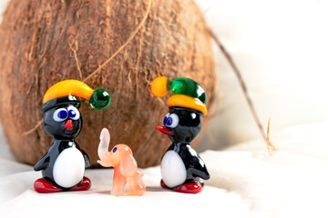 Animal figurines made from Murano glass. A pair of penguins and a pink elephant made from Venetian glass in front of a coconut. Handmade fine art. Close up.