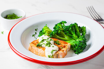 Fried salmon with creamy sauce and broccoli in white plate. Healthy food concept.