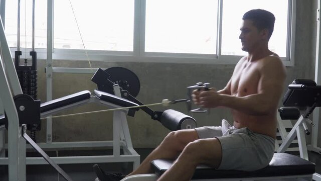 fit man shirtless exercises with  rowing machine in fitness club  . Muscular man workout  pumping up muscles chest with cable crossover at gym . bodybuilder training in sport center
