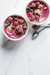 Berry smoothie bowl with granola, coconut and hemp seeds, marble background. Vegan food concept.