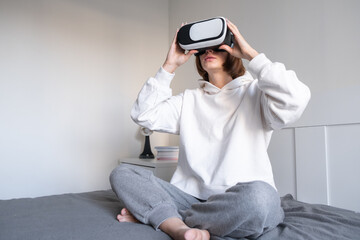 Obraz premium The girl looks into virtual reality glasses at home. A young woman plays virtual games through a special device.