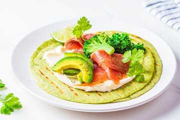 Green tortilla with broccoli, avocado, cream cheese and salted salmon on white marble background....