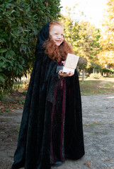 a girl in a witch costume in a cloak for Halloween with a casket