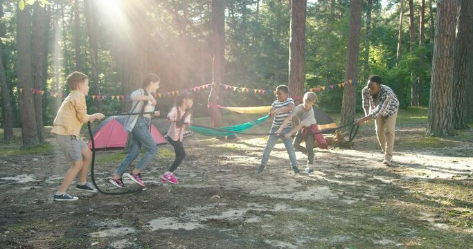 Full length view of the kids at summer camp playing tug or war with their multiracial teacher at the forest. Happy childhood and activities concept