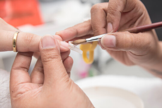 A manicurist applies acrylic to the nail and nail form with a pinch brush. At a salon or parlor.