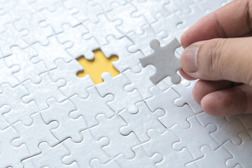 Selective focus of hand holding a piece of jigsaw puzzle and an empty space of puzzle at the back.  Business concept of solution.