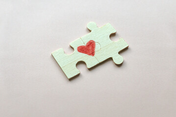 Selective focus of two pieces of a puzzle forming a heart on a pink background. Love concept.