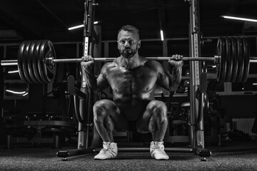 Image of a powerful athlete squatting with a barbell in a gym. Fitness and bodybuilding concept.