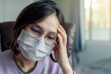 Asian woman wearing a mask sit inside the room expressing feelings of thought, anxiety, or concern