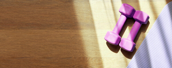 Pink fitness dumbbell and mat in the sports gym on the wooden floor. Template for sports banner...
