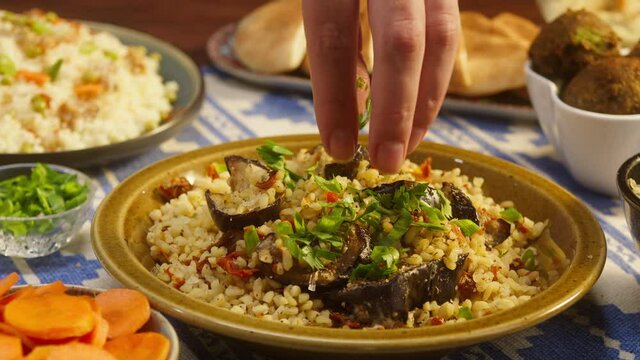 Sprinkling greenery on bulgur with eggplant close-up, couscous with meat on background. Traditional middle eastern culture. Delicious rice with meat. Arabian cuisine. Homemade food concept.