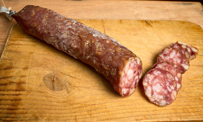 Piece of salami on a wooden board. There are several pieces cut