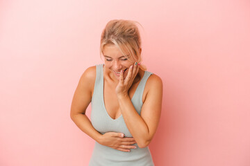 Young Russian woman isolated on pink background laughs happily and has fun keeping hands on stomach.