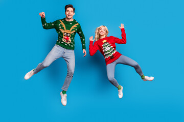 Fototapeta na wymiar Photo of pretty cheerful young couple dressed ugly print sweaters smiling jumping high isolated blue color background