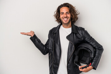 Young biker caucasian man holding a motorbike helmet isolated on gray background showing a copy...