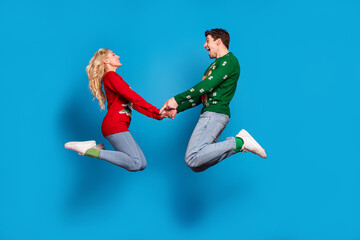 Fototapeta na wymiar Photo of impressed sweet young people wear ugly ornament pullovers jumping high holding arms isolated blue color background