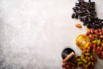 Wine bottles with grapes and wineglasses on old gray concrete table background with copy space. Red wine with a vine branch. Wine composition on rustic background. Mock up.