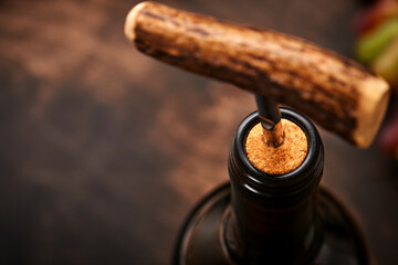Bottle wine with corkscrew. Opening a wine bottle with a corkscrew in a restaurant. Wine composition on dark rustic background with copy space. Mock up.