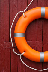 Orange life buoy hanging on red wooden wall