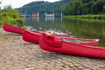 three red canoes with nile gooses and ship lock in background at an inlet for a river hike as a leisure experience on river neckar in southern Germany - obrazy, fototapety, plakaty